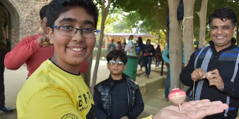 Smiling boy in a yellow shirt balances a spinning top on his palm while others watch