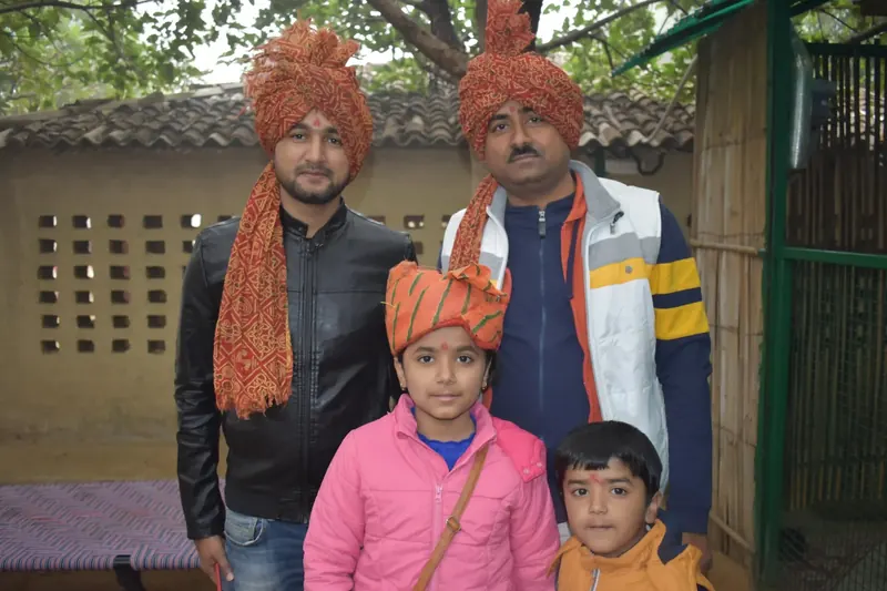 Two men and two children in orange turbans and red tilak pose together outdoors