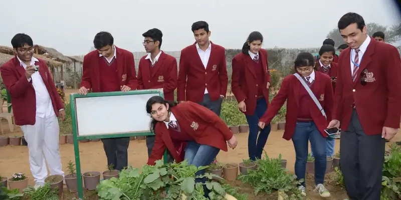 Children in maroon blazers examining potted plants beside a white board in a nursery