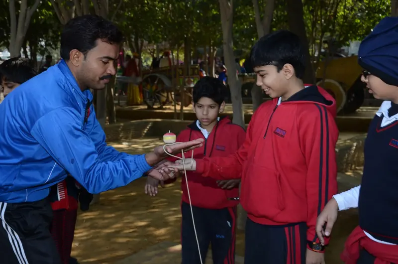 Instructor in a blue track jacket showing boys a spinning top balanced on his palm