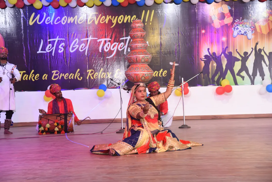 Folk dancer balancing a stack of painted pots on her head on stage while a drummer in a red turban plays beside her