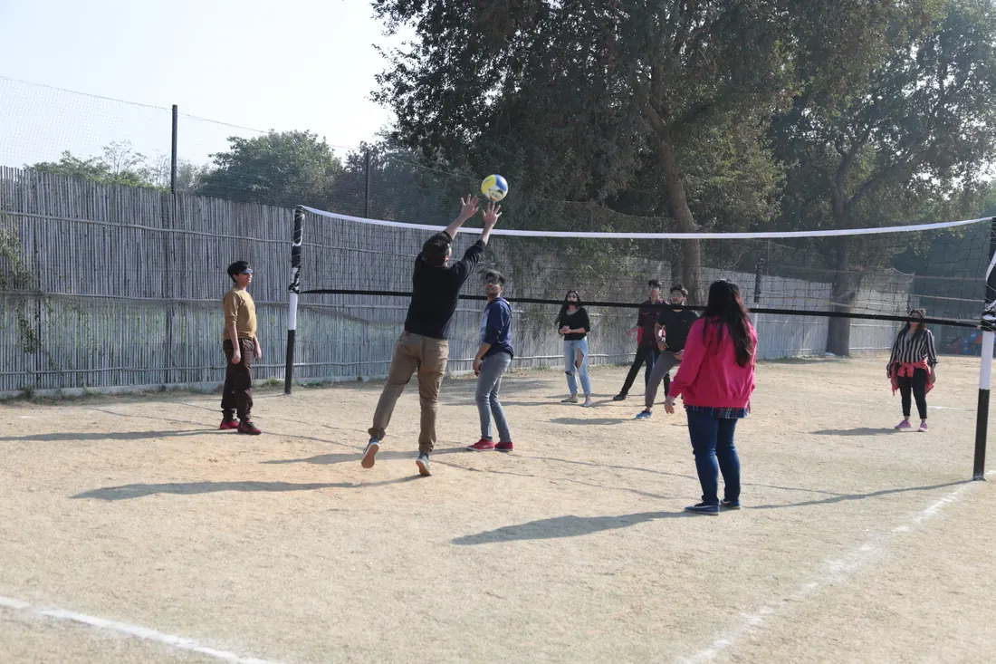 Colleagues mid-rally in a game of volleyball on the sand court while team-mates watch