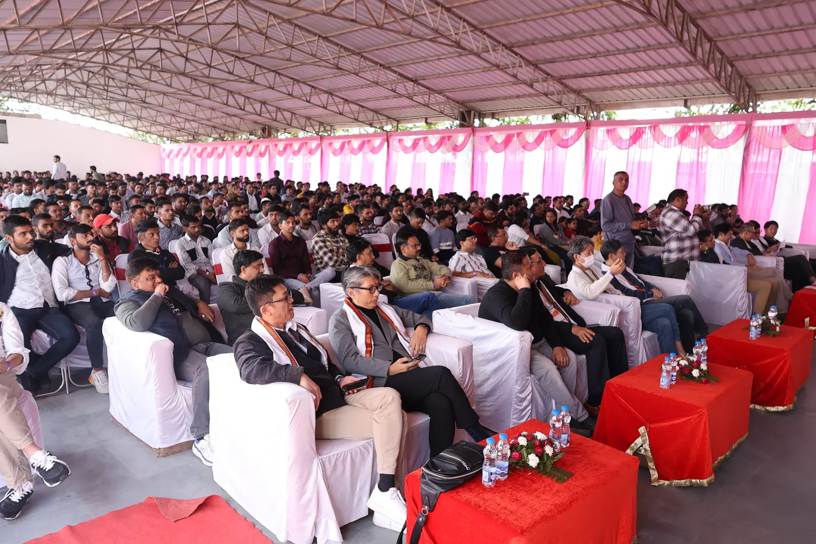 Employees seated in rows of white-covered chairs under a pink-draped pandal at a company get-together at Pratapgarh Farms