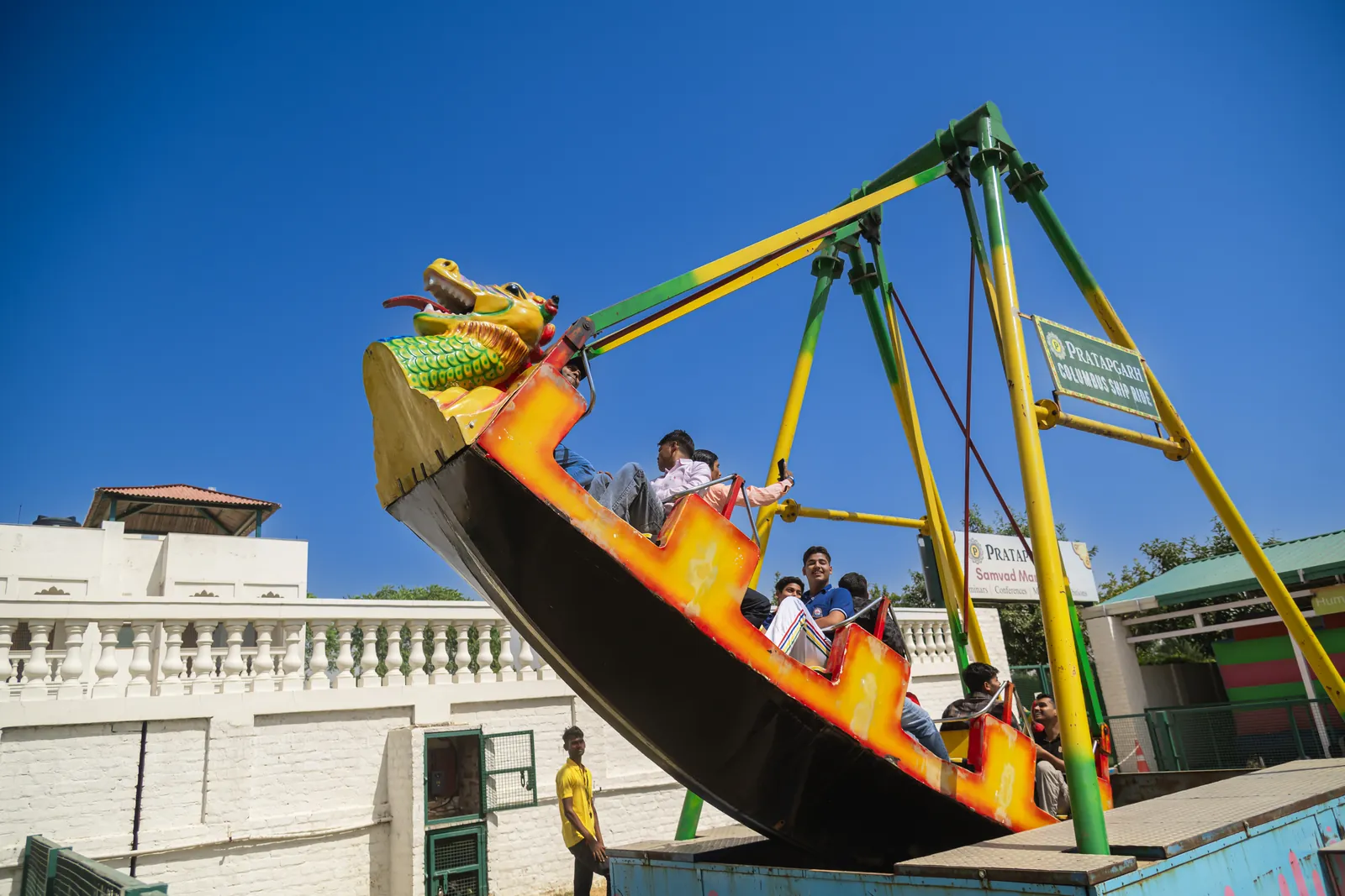 A dragon-headed ship ride swinging high on its pendulum arm with guests seated inside, above the farm's rooftops