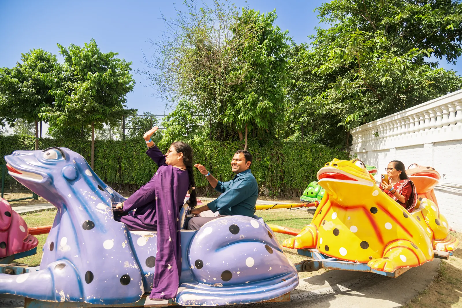 Guests riding painted blue and yellow frog-shaped cars on the Frog Ride in the carnival zone at Pratapgarh Farms