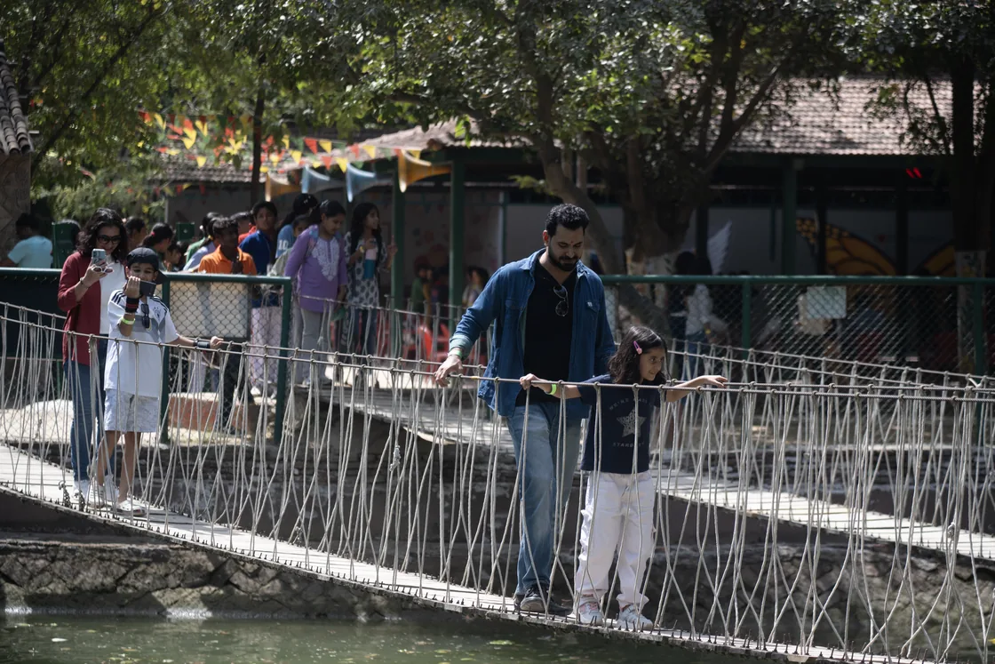 A father and his daughter holding the jute rope railings of the suspension bridge over the lake, with a queue of families behind them