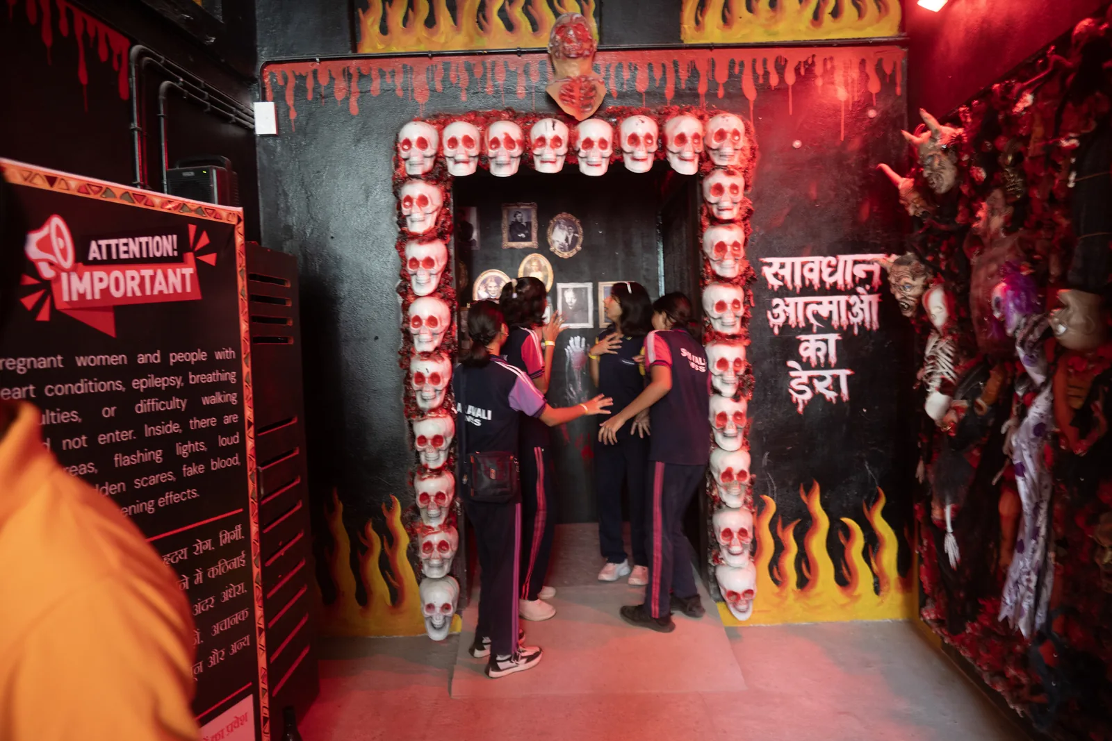 A group of schoolgirls in uniform stepping through a skull-lined doorway into the Haunted House at Pratapgarh Farms