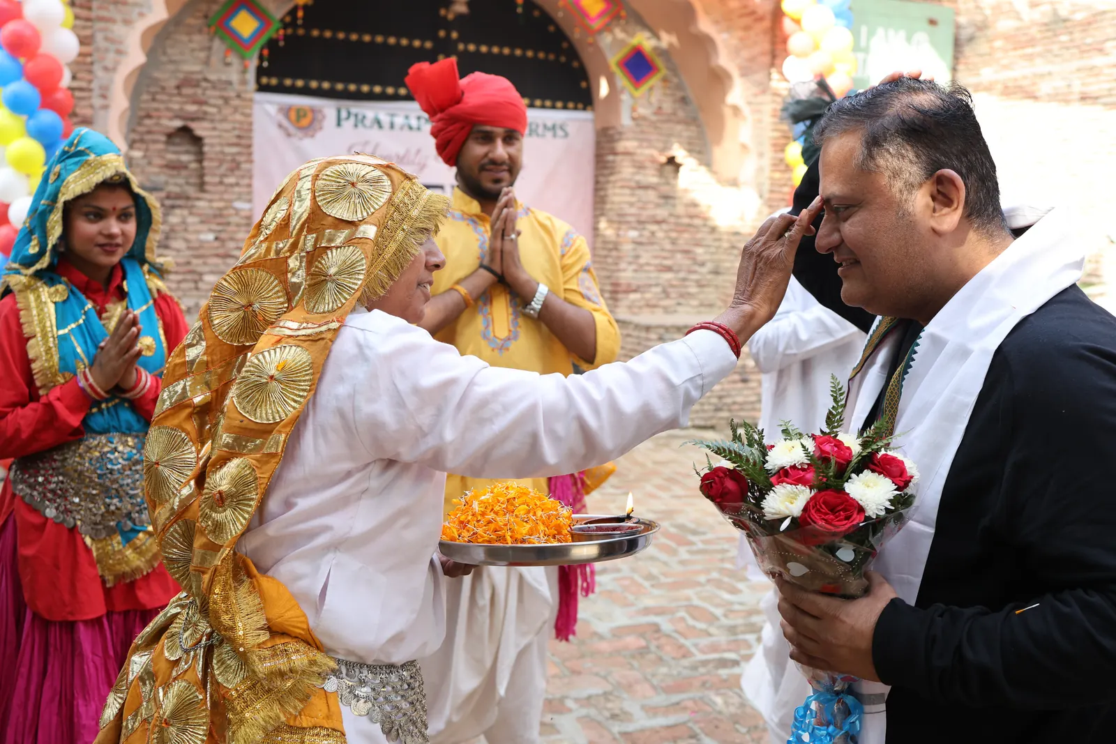 A guest being welcomed with a tilak, a garland and a bouquet by folk artists in Haryanvi dress at the farm gate