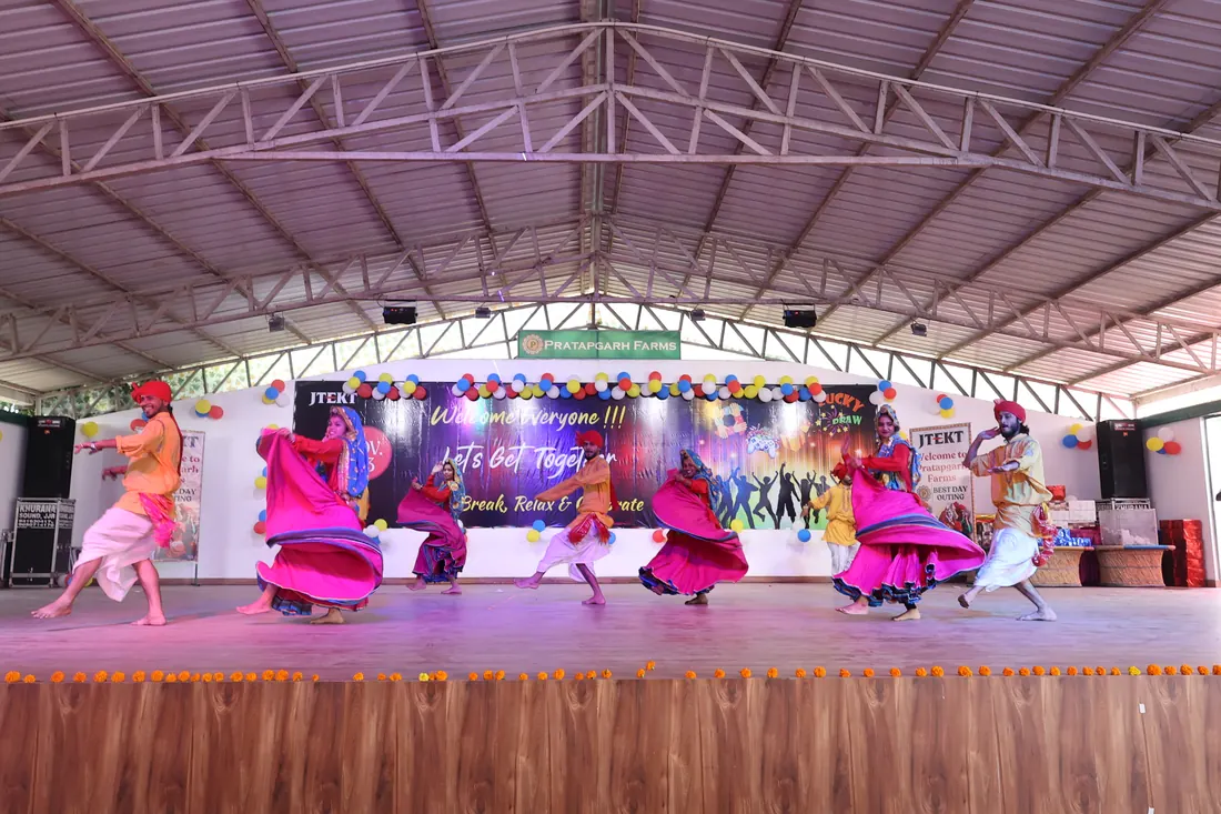 Folk dancers in bright Haryanvi dress performing on a stage with a customised corporate backdrop and balloon decor