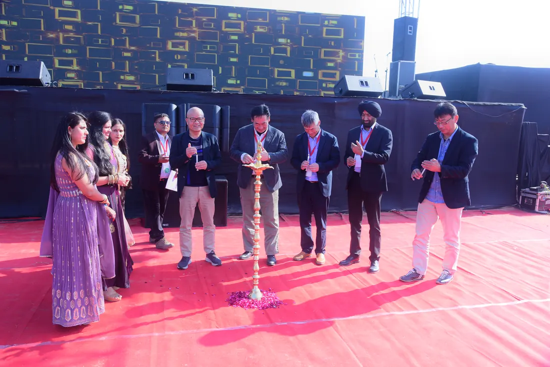 Guests in blazers lighting the ceremonial lamp on a red-carpet open-air stage