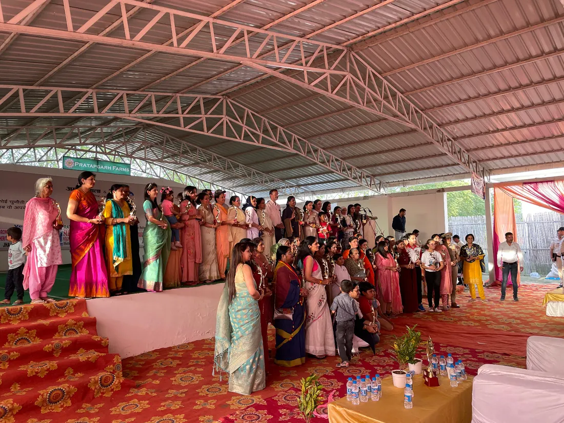 Guests being felicitated with garlands on a carpeted stage under the covered pandal