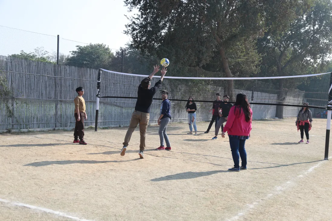 Colleagues mid-rally in a game of volleyball on the sand court while team-mates watch