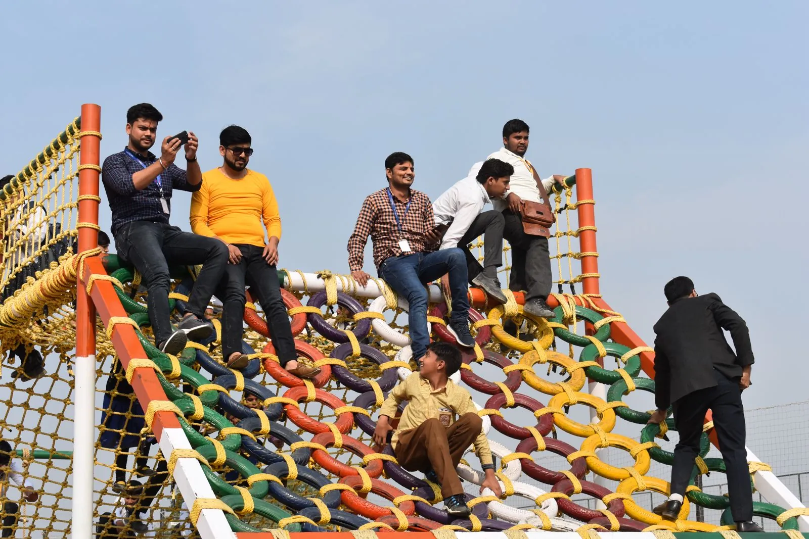 Men climbing a wide wall of coloured rope netting threaded with tyres on the adventure course