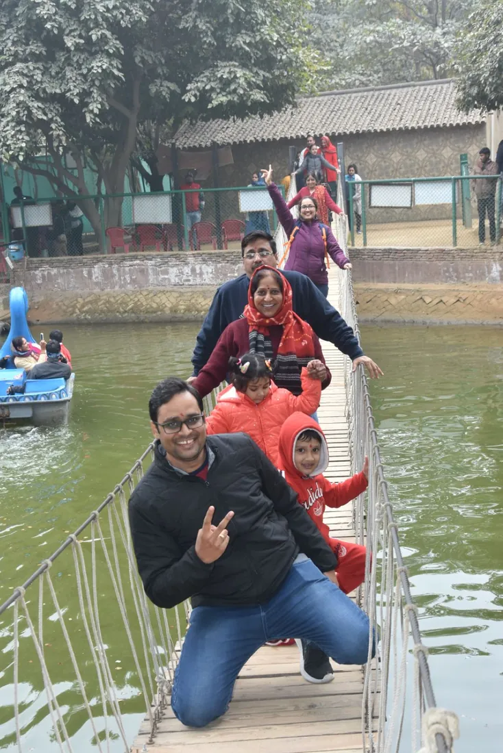 A family walking a narrow suspension bridge over the lake, with a blue pedal boat on the water beside them