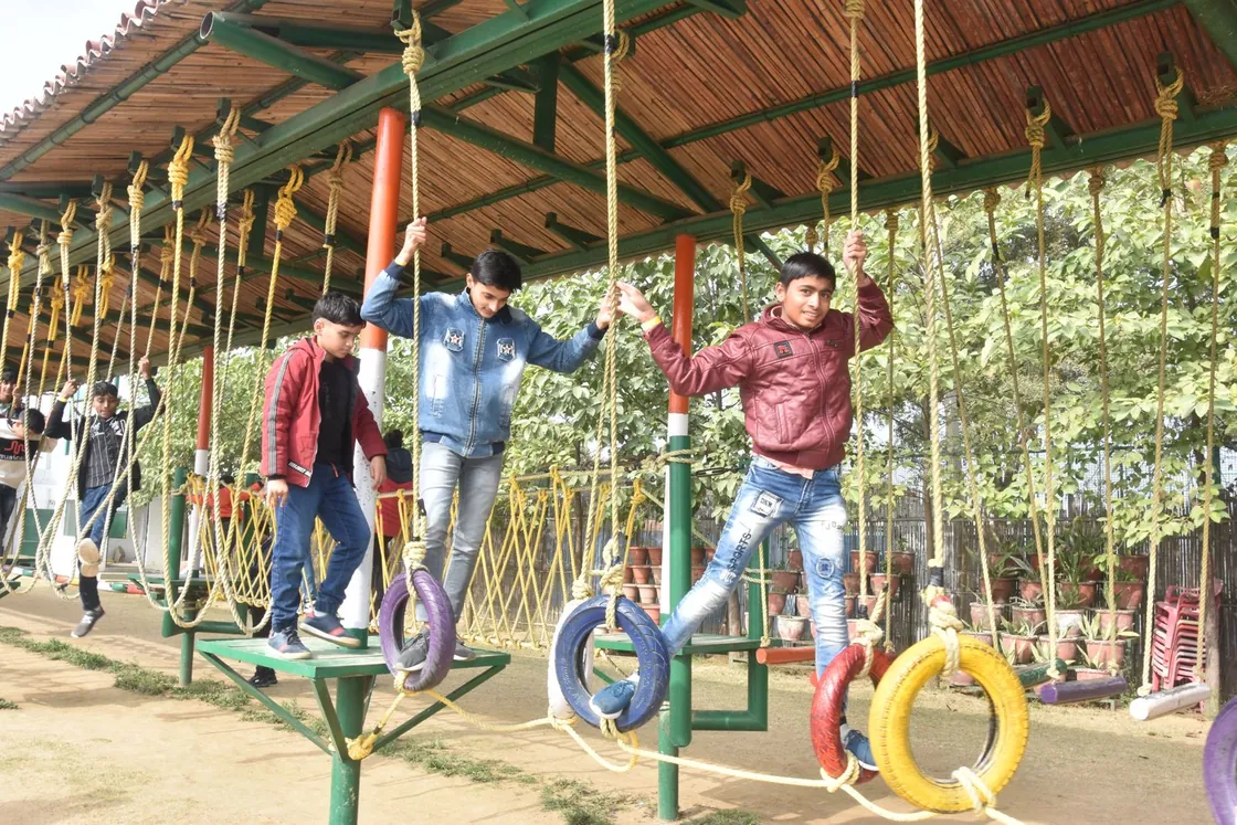 Boys stepping across painted tyres hung from ropes on a tyre traverse under a tin roof