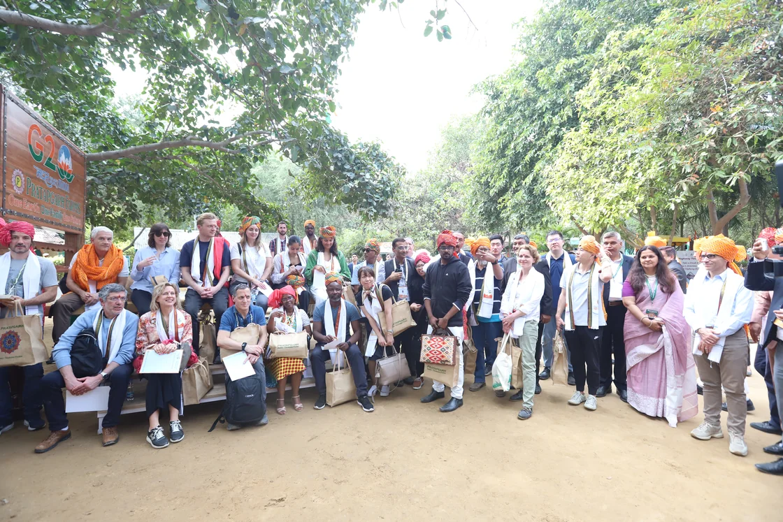 The G20 delegation and the Pratapgarh Farms team gathered on and around a tractor trolley, most of them wearing Haryanvi pagdis, beside the farm's G20 board