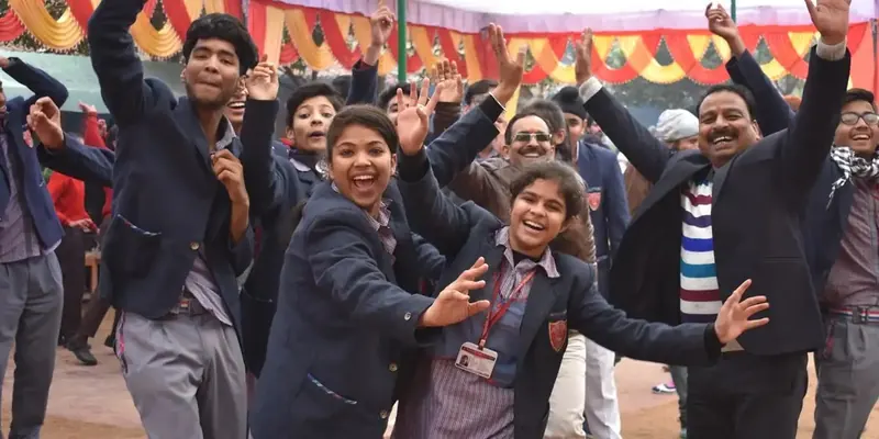School students in navy blazers cheering with their arms raised under a colourful canopy of bunting
