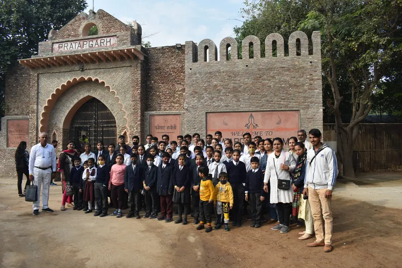 A large school group posing for a photograph before the brick arch and welcome sign at the farm entrance