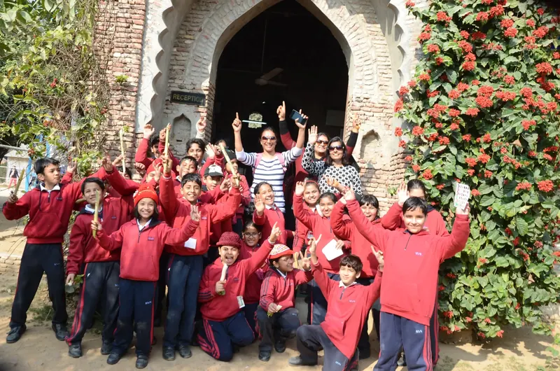 Students in red tracksuits cheering with their arms raised outside the farm's brick archway